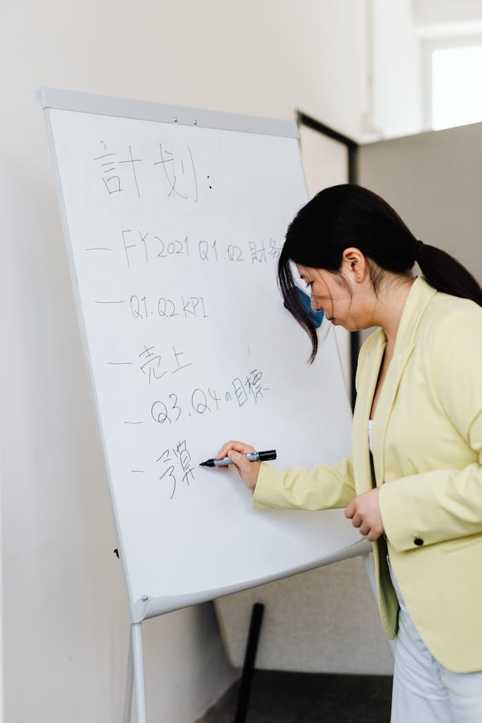 Asian businesswoman writing on a whiteboard during a presentation in a corporate setting.